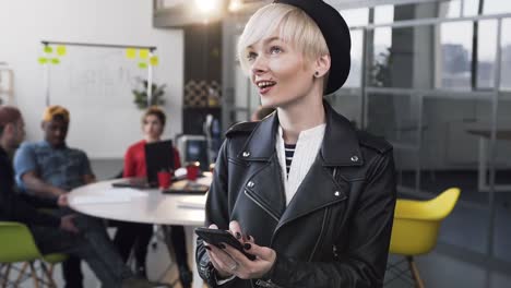 Atractiva-mujer-de-negocios-trabajando-en-el-teléfono-inteligente-con-un-grupo-de-jóvenes-empresarios-en-el-fondo