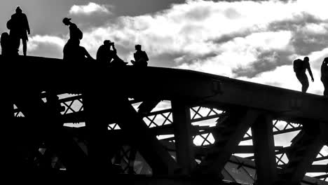 silhouettes-of-young-people-strolling-and-taking-pictures-of-each-other-in-a-precarious-situation-on-the-top-of-the-bridge,-time-lapse