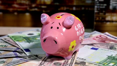 Pink-piggy-bank-on-rotating-surface-with-dollars-and-euro-banknotes.