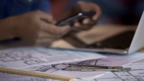 Apartment-layouts-lying-on-table,-female-architect-typing,-scrolling-on-phone