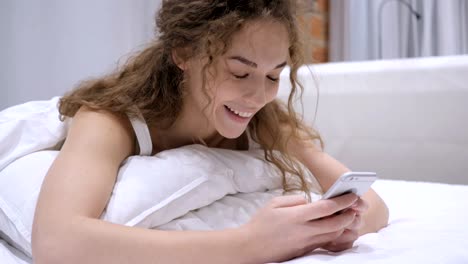 Mujer-tumbada-en-la-cama-usando-el-teléfono-para-la-navegación-en-línea