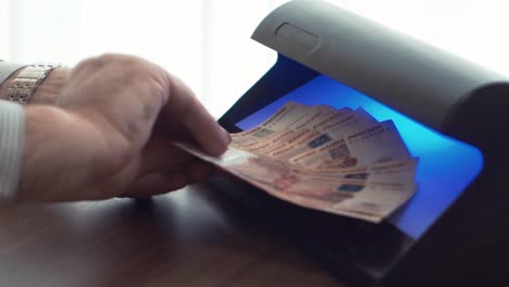 Businessman-hand-checking-five-thousand-ruble-banknote-on-uv-light-detector