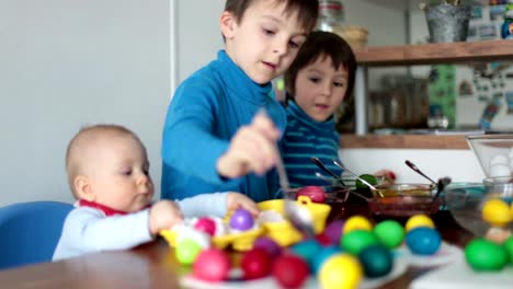 Three-children,-brothers,-coloring-and-painting-easter-eggs-at-home-in-kitchen-for-the-holiday