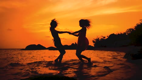 dos-chicas-baila-felices-cogidos-de-la-mano-en-la-playa-al-atardecer-en-cámara-lenta