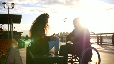 Pareja-feliz---hombre-joven-discapacitado-en-silla-de-ruedas-con-mujer-joven-disfrutar-de-la-puesta-de-sol-juntos