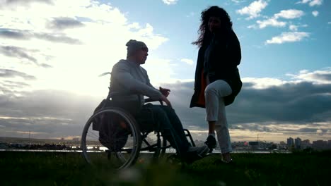 Care-of-disabled---man-in-a-wheelchair-with-woman-talking-at-the-cloudy-sunset