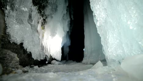 Eishöhle-des-Baikalsees-Frau-unterwegs.-Ausflug-nach-Winter-Island.-Mädchen-Backpacker-ist-von-Eis-Grot-Fuß.-Am-schönen-Eisgrotte-sucht-Reisende.-Wanderer-trägt-silberne-Jacke,-Rucksack,-led-Lampe.