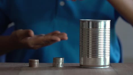 Woman-drop-a-coin-into-a-old-can-on-table.