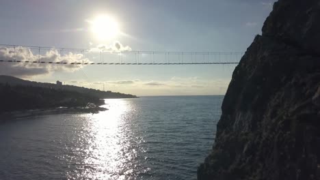 Luftaufnahme-der-Hängebrücke-zwischen-den-Felsen-über-dem-Meer-und-Gefahr-Wellen-und-Steinen