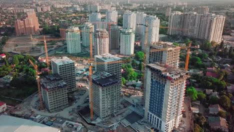 Aerial-drone-shot.-Construction-of-high-rise-buildings-in-the-developing-area-of-a-large-city.-In-the-picture,-construction-cranes-and-many-houses-under-construction.-Around-the-construction-site-to-the-right