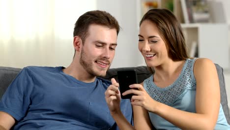 Happy-couple-talking-about-phone-content-at-home