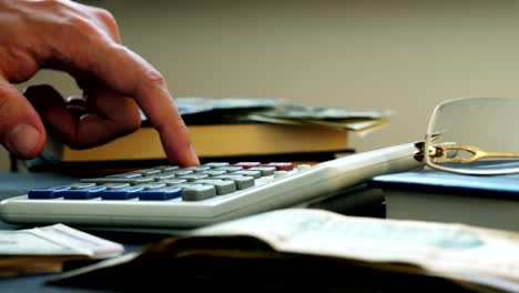 Hand-counting-on-a-calculator-and-money-on-a-desk.