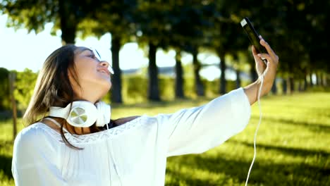 Beautiful-girl-taking-selfie-video-using-smartphone-outdoors-Girl-sharing-photograph-on-social-media-with-mobile-phone