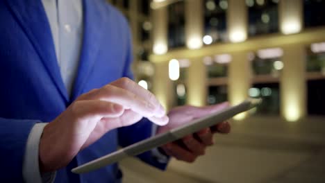 Close-up-hands-of-unrecognizable-businessman-using-application-on-digital-tablet-outdoors-at-night