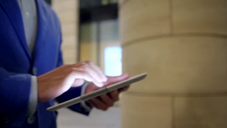 Hands-of-businessman-using-tablet-computer-while-walking-down-city-street-in-night,-close-up