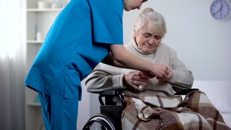 Joven-enfermera-dando-medicamentos-a-anciana-en-silla-de-ruedas,-centro-de-rehabilitación