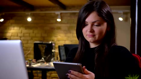 Closeup-portrait-of-adult-caucasian-businesswoman-using-tablet-in-front-of-the-laptop-in-the-office