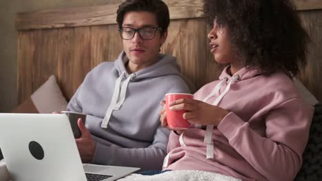 Young-couple-drinking-coffee-and-using-laptop-in-bed