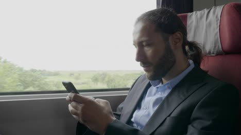 Young-entrepreneur-man-commuter-on-train-sitting-next-the-window-using-smartphone-on-his-way-to-office