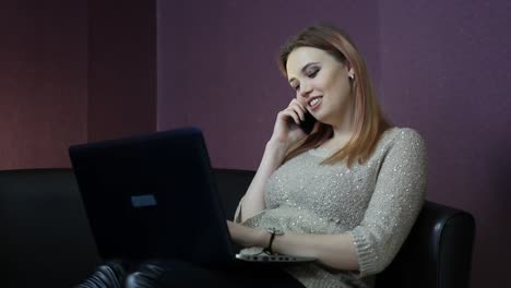 A-young-woman-works-at-a-computer-while-sitting-on-a-small-couch.