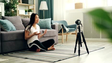 Joyful-Asian-woman-popular-blogger-is-recording-video-using-professional-camera-talking-then-showing-thumbs-up-and-waving-hand-to-her-followers.-Vlogging-and-technology-concept.