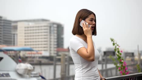 Beautiful-asian-woman-talk-to-cellphone-beside-river.-Attractive-and-cheerful-young-asian-female,-Slow-motion-shoot.