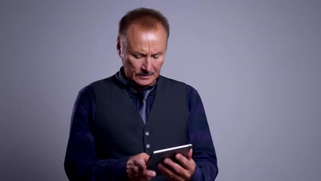 Closeup-portrait-of-concentrated-senior-caucasian-man-typing-on-the-tablet-with-the-background-isolated-on-gray