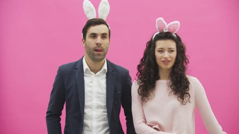 Young-couple-standing-standing-on-pink-background.-During-this-time,-they-are-dressed-in-rabble-ears.-Looking-at-each-other-smiles-sincerely