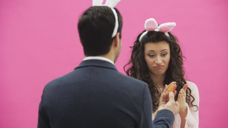 Beautiful-young-girl-standing-on-a-pink-background.-During-this,-there-are-ears-of-rabbits-on-the-head.-A-man-stands-back-to-the-camera,-holding-a-carrot-showing-the-girl.-The-girl-does-not-like-carrots,-leaving-the-frame.-The-man-looks-in-the-frame.