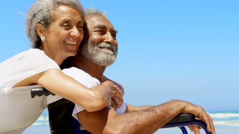 Side-view-of-active-senior-African-American-woman-embracing-disabled-senior-man-on-the-beach-4k