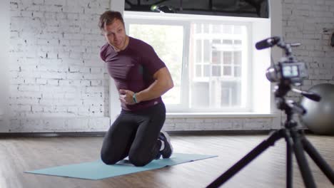 Entrenador-en-línea-hablando-en-cámara-y-mostrando-ejercicio-de-tablón-en-el-gimnasio