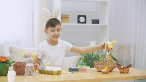 Young-and-smily-boy-is-taking-a-wooden-basket-and-shows-how-many-coloured-Easter-eggs-there-are,-and-raises-his-thumb-finger-up,-twicely.