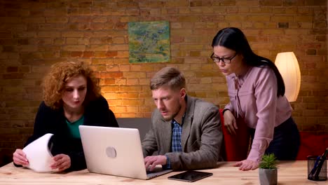 Closeup-shoot-of-young-businessman-working-on-the-laptop-getting-happy-and-celebrating-success-with-two-female-colleagues.-Businesswoman-holding-a-tablet