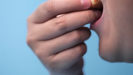 Asian-preteen-boy-eating-donut-with-blue-background,-side-view-and-slow-motion..