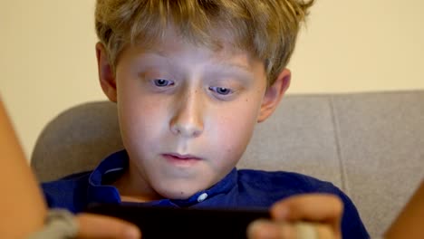 4K-boy-sitting-on-couch-playing-his-smartphone