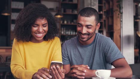 Young-couple-watching-video-on-mobile-phone-and-laughing