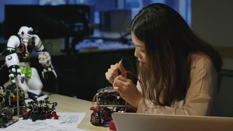 Young-asian-female-electronics-development-engineers-works-with-robot,-measuring-the-signal-in-the-electrical-circuits-of-robotics-prototype-in-workshop.-People-with-technology-or-innovation-concept.