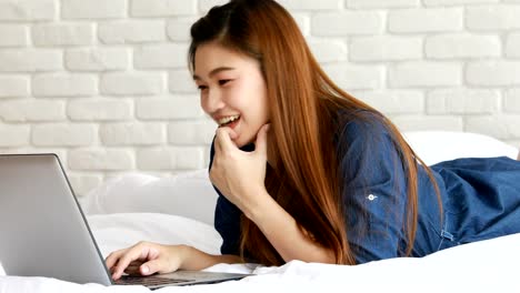 Beautiful-Attractive-Asian-young-woman-lying-on-bed-and-using-computer-laptop-for-using-social-media-and-shopping-online-relax-in-bedroom-in-holiday,Lifestyle-in-bedroom-Concept