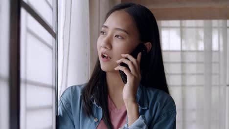 Portrait-smiling-young-asian-woman-talking-on-Phone-with-friends-standing-beside-window-at-home-office.