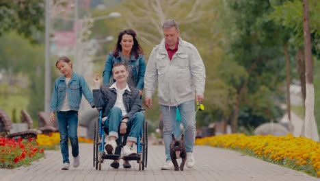 Happy-family-spends-the-day-together-for-a-walk-in-the-park.-Young-man-with-disabilities-walks-with-his-parents,-sister-and-dog.