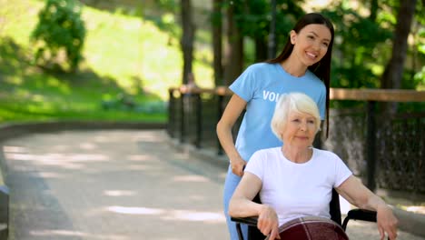 Happy-social-volunteer-walking-hospital-garden-with-disabled-elderly-pensioner