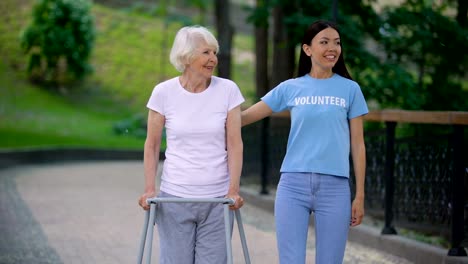 Fürsorgliche-junge-Frau-unterstützt-alte-Dame-mit-Spazierrahmen,-soziale-Freiwilligenarbeit