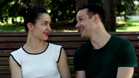 A-young-beautiful-girl-and-her-handsome-young-boyfriend-watch-the-news-in-the-social-network-on-their-smartphone-while-sitting-on-a-park-bench.