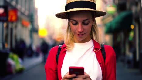 Close-up-portrait-of-authentic-Caucasian-female-standing-with-smartphone-in-hands-and-sincerely-smiling-for-camera