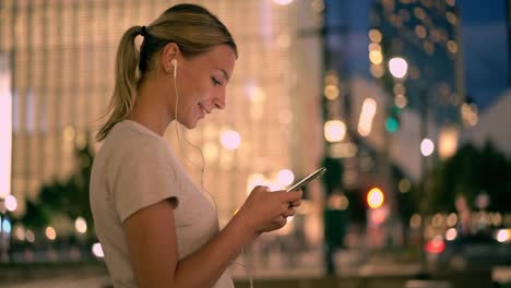 Meloman-femenino-positivo-buscando-nuevas-pistas-de-audio-a-través-de-la-aplicación-multimedia-en-celular-para-escuchar-música-durante-caminar