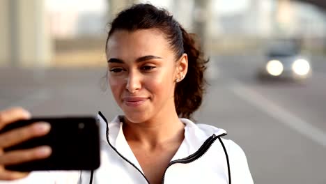 Mujer-joven-en-ropa-deportiva-tomando-selfie-con-su-teléfono-móvil.-Feliz-relajación-femenina-después-del-entrenamiento.