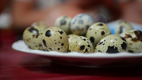 Female-hand-takes-small-quail-egg-from-the-plate-on-table-at-night-asian-market.-Closeup-of-fresh-quail-eggs