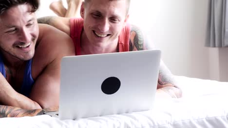 Gay-couple-in-bed-using-laptop-computer.-Small-sweet-talk.