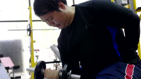 Asian-man-trying-to-exercise-with-dumbbell-in-fitness-gym,-Healthy-lifestyle,-weight-loss-desire