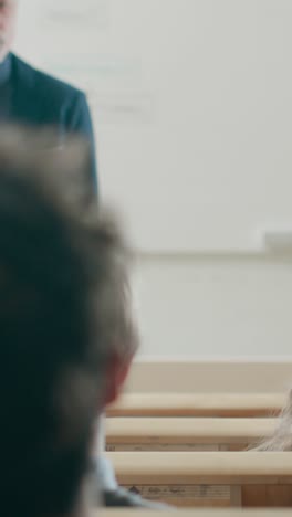 Back-View-of-the-Students-in-the-Lecture-Hall,-Listening-to-a-Professor-Giving-a-Lecture,-One-Student-Raises-Hand-and-Asks-Question.-Video-Footage-with-Vertical-Screen-Orientation-9:16